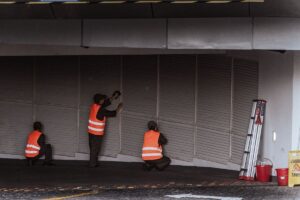 Pekerja memasang rolling door di pintu masuk gedung sebagai ilustrasi pekerjaan facility management yang terdokumentasi