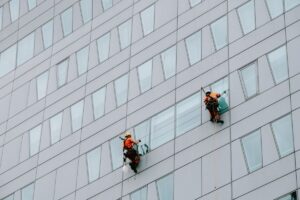 Pekerja rope access membersihkan jendela gedung modern sebagai ilustrasi pemeliharaan gedung hotel