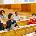 Dosen berdiri di depan mahasiswa dalam ruang kelas sebagai simbol sistem manajemen organisasi pendidikan ISO 21001