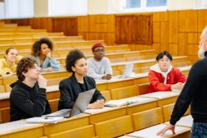 Dosen berdiri di depan mahasiswa dalam ruang kelas sebagai simbol sistem manajemen organisasi pendidikan ISO 21001