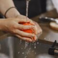 Tangan mencuci bahan pangan mentah di bawah air mengalir sebagai simbol program prasyarat higiene ISO 22001