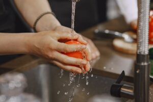 Tangan mencuci bahan pangan mentah di bawah air mengalir sebagai simbol program prasyarat higiene ISO 22001
