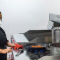 Juru masak bekerja dengan masker pelindung di dapur komersial sebagai simbol kompetensi dan training ISO 22001